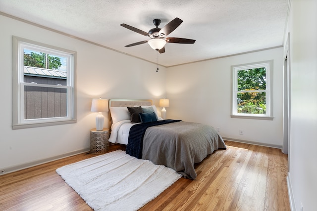 bedroom featuring ceiling fan, a textured ceiling, light wood-type flooring, and crown molding