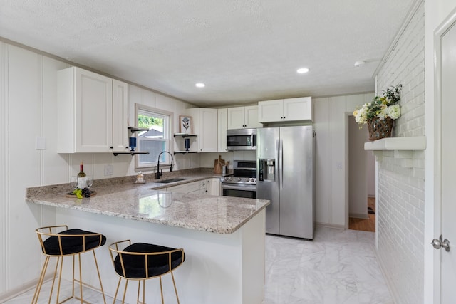 kitchen with appliances with stainless steel finishes, a textured ceiling, sink, white cabinets, and kitchen peninsula