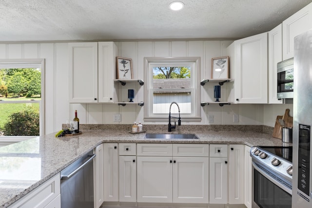 kitchen with stainless steel appliances, light stone counters, white cabinets, a textured ceiling, and sink