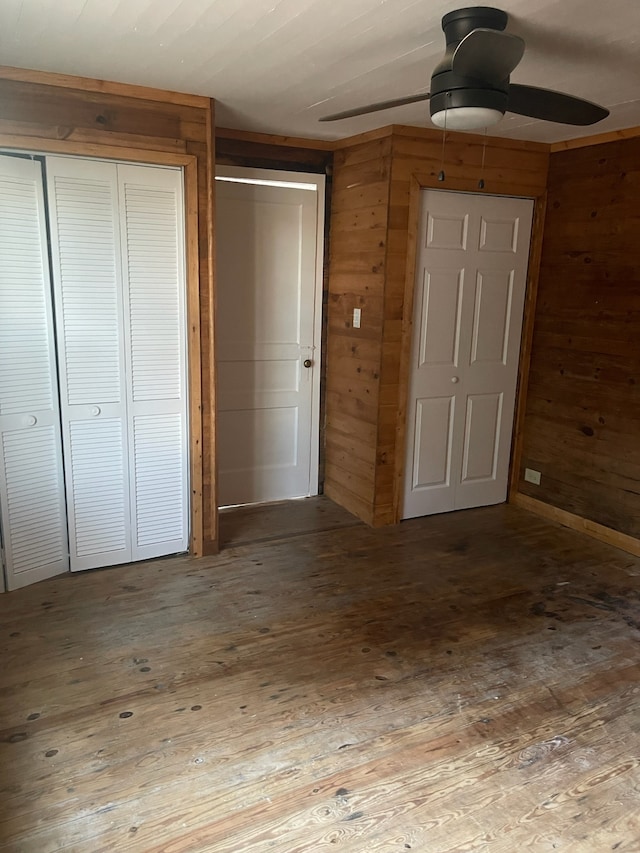 unfurnished bedroom featuring ceiling fan, wood-type flooring, wooden walls, and a closet