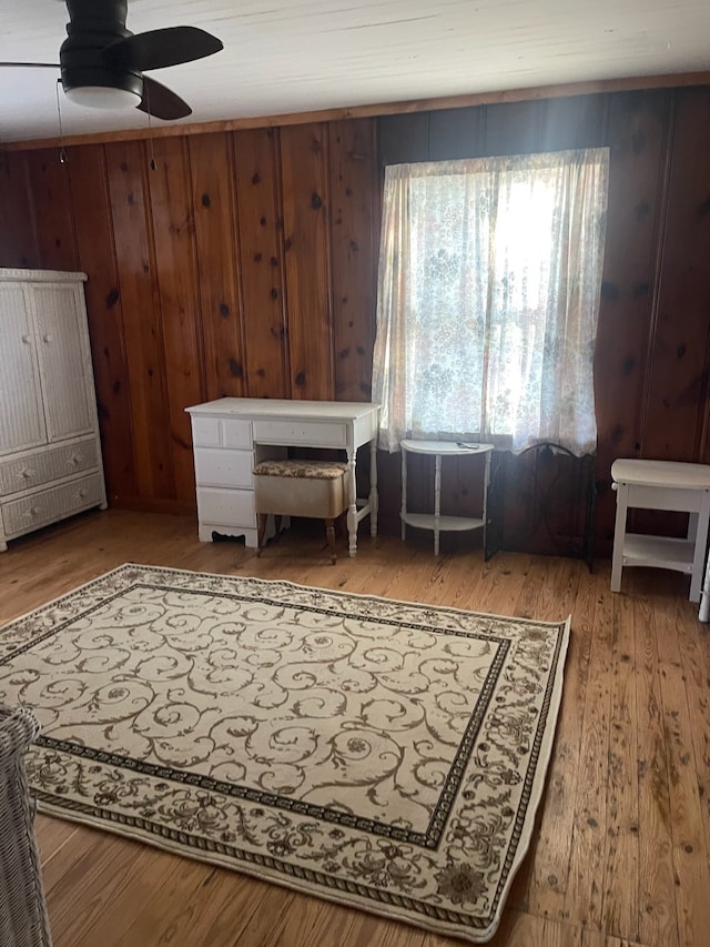 sitting room featuring hardwood / wood-style flooring, ceiling fan, and wooden walls