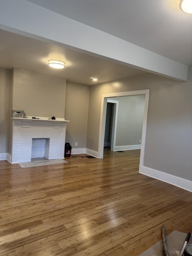 unfurnished living room with beamed ceiling, wood-type flooring, and a brick fireplace