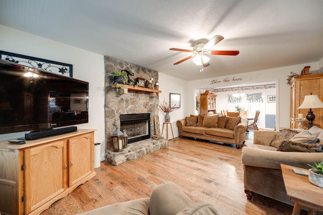 living room with a textured ceiling, light wood-type flooring, a fireplace, and ceiling fan