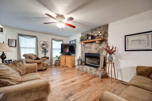 living room with a fireplace, ceiling fan, a textured ceiling, and light hardwood / wood-style flooring