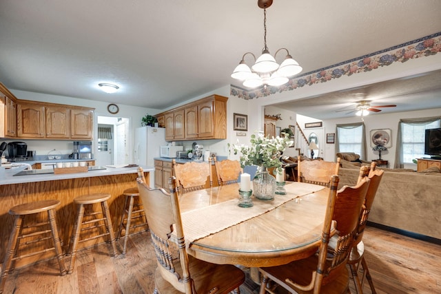 dining space with hardwood / wood-style flooring, ceiling fan with notable chandelier, and sink