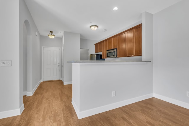 kitchen with kitchen peninsula, appliances with stainless steel finishes, and light hardwood / wood-style floors