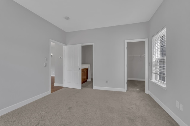 unfurnished bedroom with light colored carpet, multiple windows, and a walk in closet