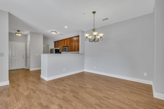 kitchen with stainless steel appliances, light hardwood / wood-style floors, kitchen peninsula, an inviting chandelier, and hanging light fixtures