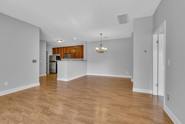 unfurnished living room featuring an inviting chandelier and light hardwood / wood-style flooring