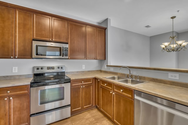 kitchen with stainless steel appliances, sink, a chandelier, pendant lighting, and light hardwood / wood-style flooring