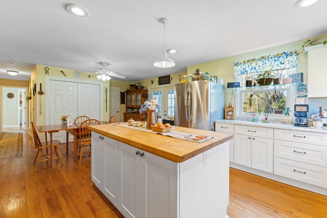 kitchen with white cabinets, a kitchen island, light hardwood / wood-style floors, butcher block counters, and stainless steel refrigerator