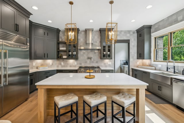 kitchen featuring stainless steel appliances, wall chimney exhaust hood, hanging light fixtures, light hardwood / wood-style flooring, and a center island