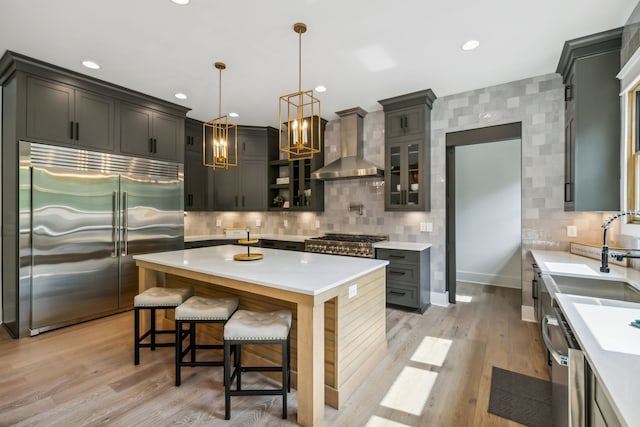 kitchen featuring stainless steel appliances, light hardwood / wood-style floors, wall chimney exhaust hood, a center island, and pendant lighting