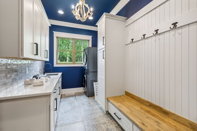 mudroom featuring stacked washer / dryer, ornamental molding, light tile patterned floors, sink, and a chandelier