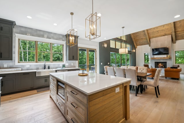 kitchen featuring sink, a fireplace, vaulted ceiling with beams, stainless steel microwave, and pendant lighting