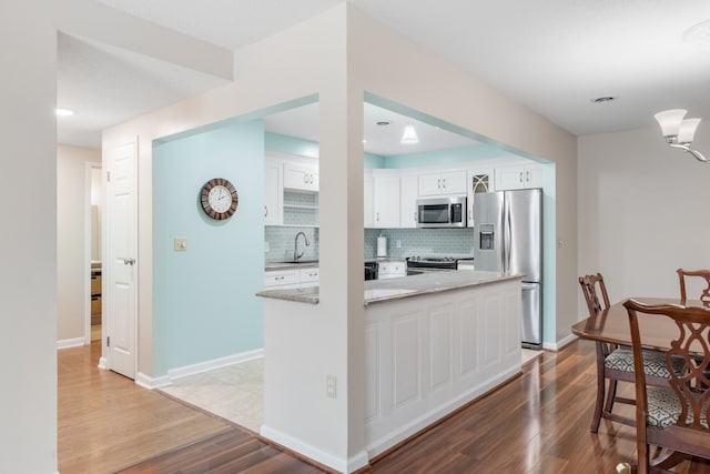 kitchen featuring stainless steel appliances, white cabinetry, light stone counters, tasteful backsplash, and light wood-type flooring