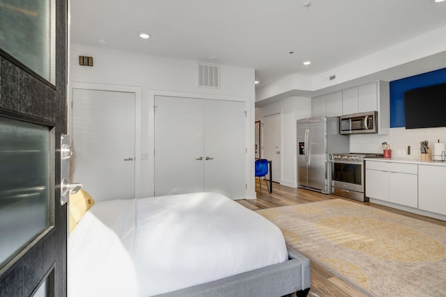 bedroom with multiple closets, stainless steel fridge with ice dispenser, and light hardwood / wood-style floors