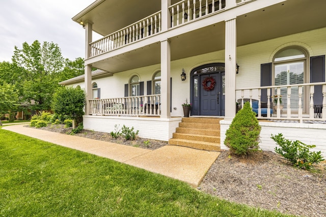 property entrance with a porch, a lawn, and a balcony