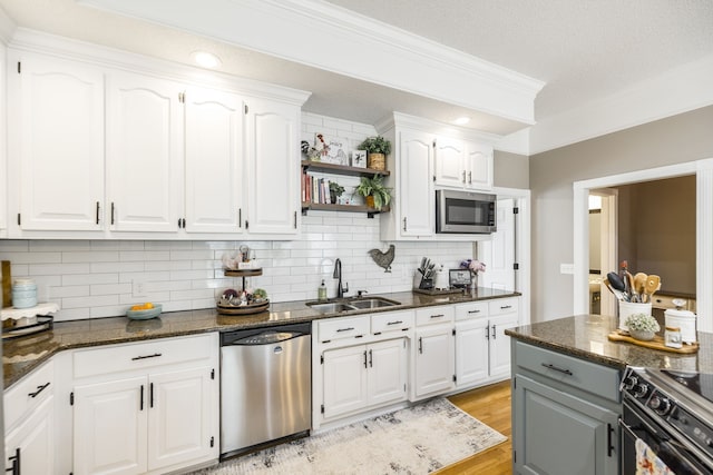 kitchen featuring stainless steel appliances, dark stone counters, light wood-type flooring, sink, and white cabinets