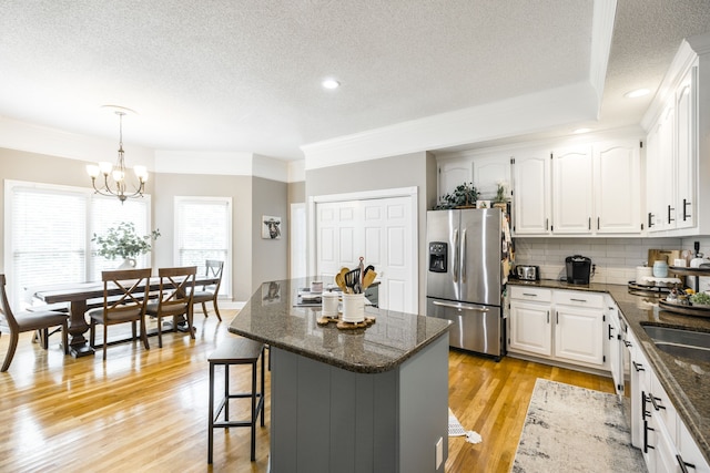 kitchen featuring light hardwood / wood-style floors, white cabinets, a kitchen island, decorative light fixtures, and stainless steel fridge