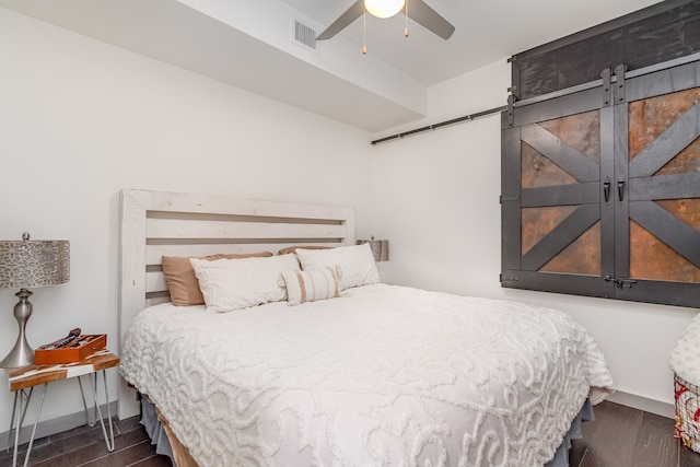 bedroom featuring a barn door, ceiling fan, and dark wood-type flooring