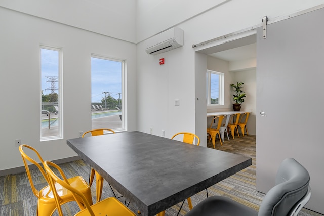 dining room featuring an AC wall unit, a wealth of natural light, a barn door, and hardwood / wood-style flooring