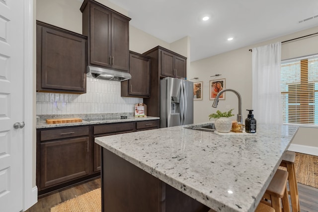 kitchen with stainless steel fridge, a kitchen island with sink, and dark wood-type flooring