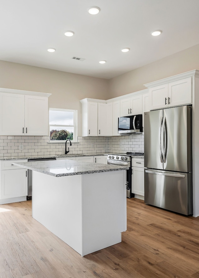 kitchen featuring stainless steel appliances, a center island, light stone countertops, white cabinetry, and light wood-type flooring