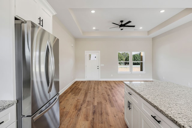 kitchen with white cabinets, light hardwood / wood-style floors, stainless steel refrigerator, and light stone countertops