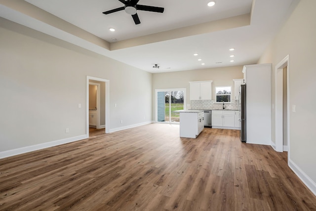 unfurnished living room featuring ceiling fan, a tray ceiling, and light hardwood / wood-style floors