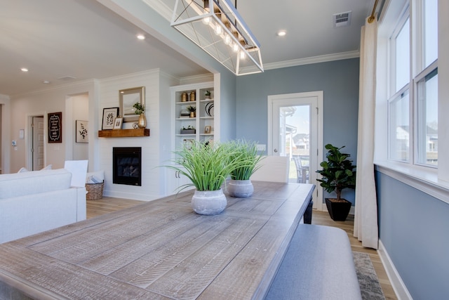 dining area with a large fireplace, light hardwood / wood-style floors, and crown molding