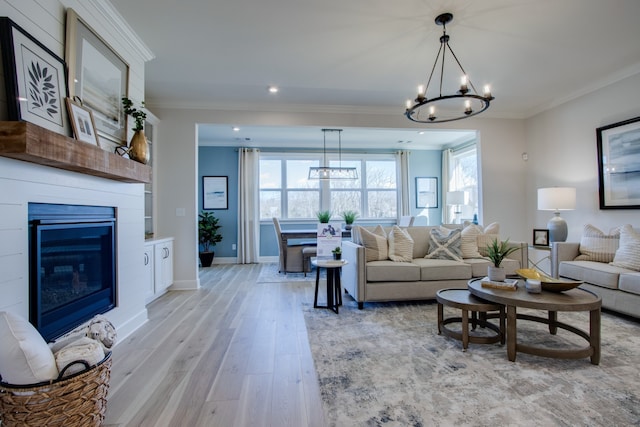 living room with a fireplace, light hardwood / wood-style floors, crown molding, and a notable chandelier