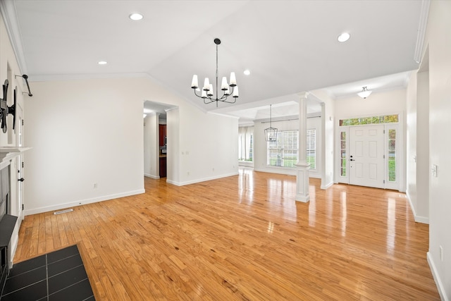 unfurnished living room featuring crown molding, a notable chandelier, ornate columns, vaulted ceiling, and light hardwood / wood-style flooring