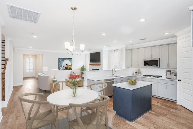 kitchen with a center island, crown molding, light hardwood / wood-style floors, decorative light fixtures, and appliances with stainless steel finishes