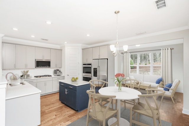 kitchen featuring stainless steel appliances, blue cabinets, sink, pendant lighting, and light hardwood / wood-style flooring