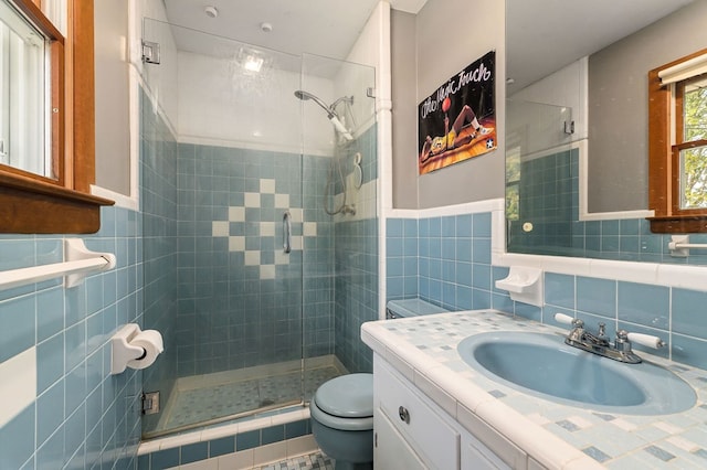 bathroom with a shower with shower door, vanity, toilet, and tile walls