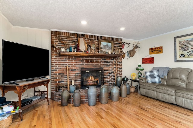 living room featuring a fireplace, a textured ceiling, light wood-type flooring, and ornamental molding