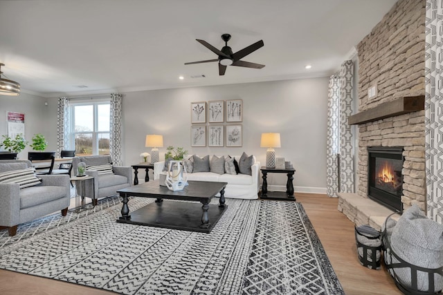 living room with hardwood / wood-style flooring, a stone fireplace, ceiling fan, and ornamental molding