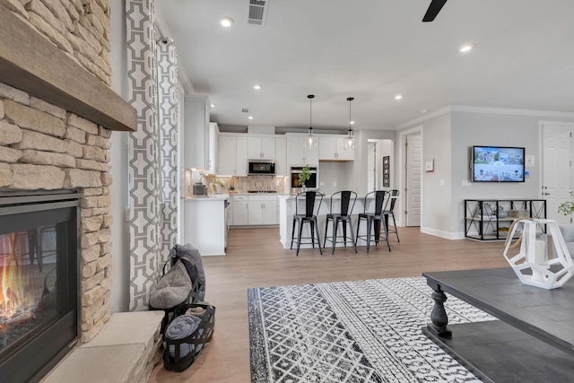 living room with a stone fireplace, crown molding, and light wood-type flooring