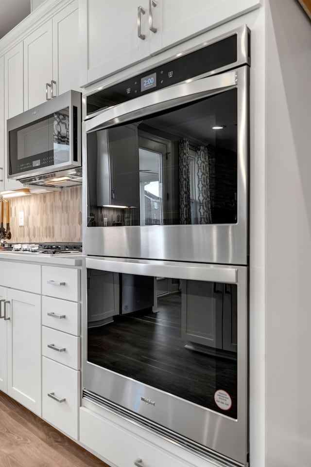 kitchen featuring tasteful backsplash, white cabinetry, light hardwood / wood-style floors, and appliances with stainless steel finishes