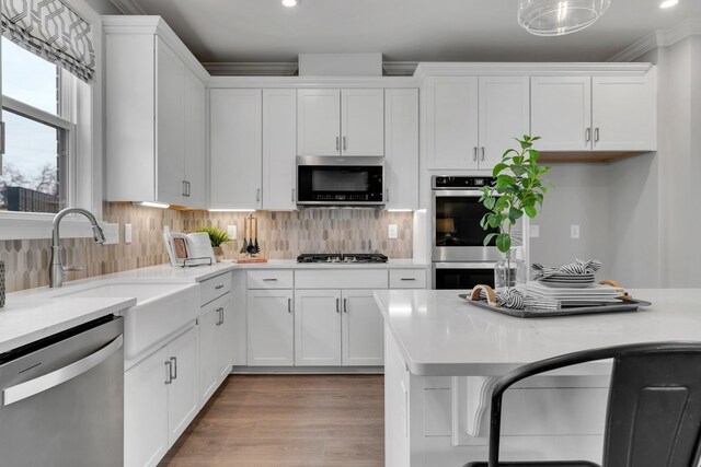 kitchen with light wood-type flooring, stainless steel appliances, white cabinetry, and backsplash