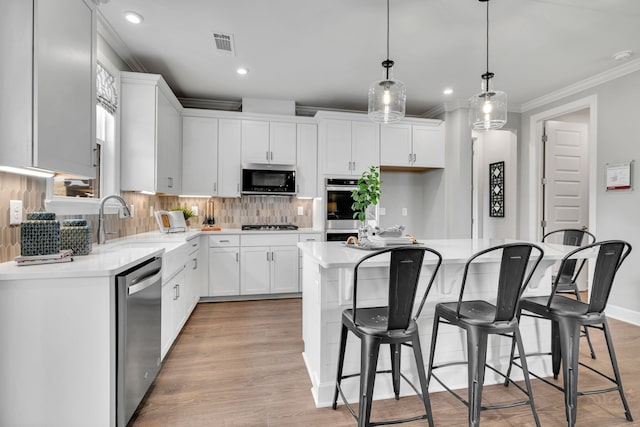 kitchen featuring appliances with stainless steel finishes, decorative light fixtures, white cabinets, light hardwood / wood-style floors, and a kitchen island