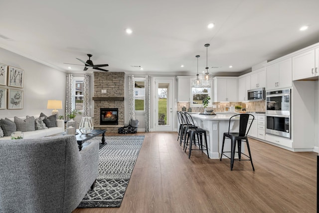 living room with crown molding, a fireplace, ceiling fan, and light wood-type flooring