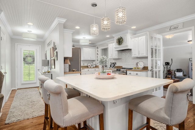 kitchen featuring ornamental molding, white cabinetry, appliances with stainless steel finishes, decorative backsplash, and light hardwood / wood-style floors