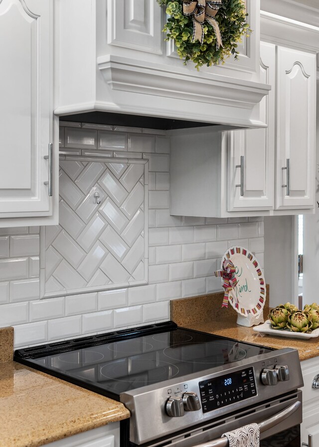 kitchen featuring white cabinetry, backsplash, light stone countertops, and electric range