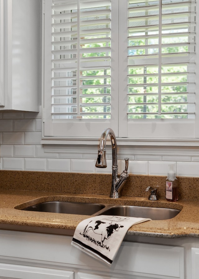 interior details with tasteful backsplash, stone countertops, sink, and white cabinets