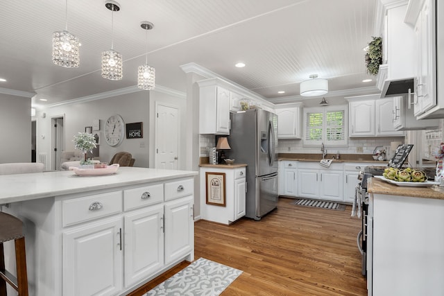 kitchen with light hardwood / wood-style floors, decorative light fixtures, crown molding, white cabinets, and stainless steel fridge with ice dispenser