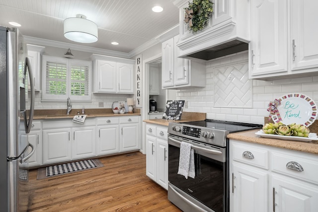 kitchen with white cabinetry, appliances with stainless steel finishes, wood-type flooring, crown molding, and premium range hood