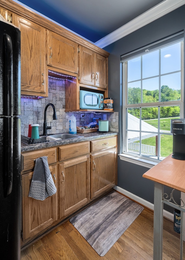 kitchen featuring light hardwood / wood-style floors, sink, black fridge, ornamental molding, and decorative backsplash