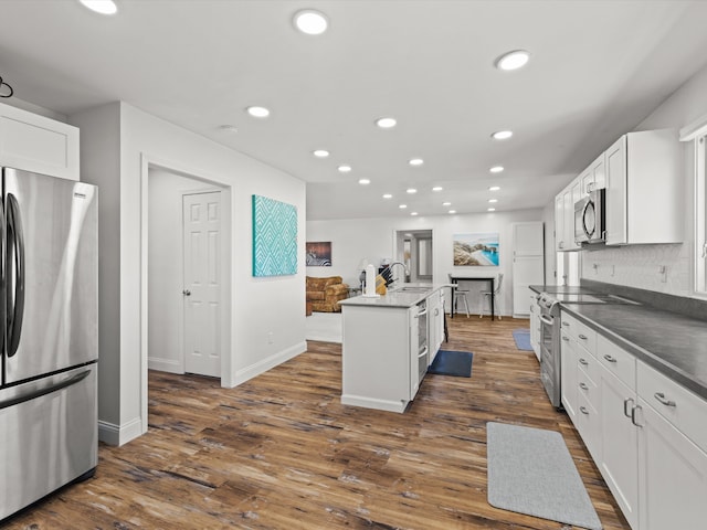 kitchen with white cabinets, appliances with stainless steel finishes, dark wood-type flooring, and a kitchen island with sink